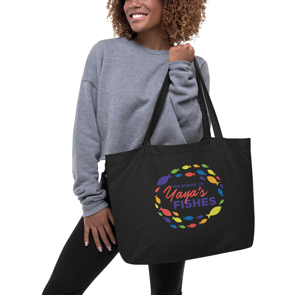 Description: Model smiling and holding Black tote bag with The School of Yaya’s Fishes logo